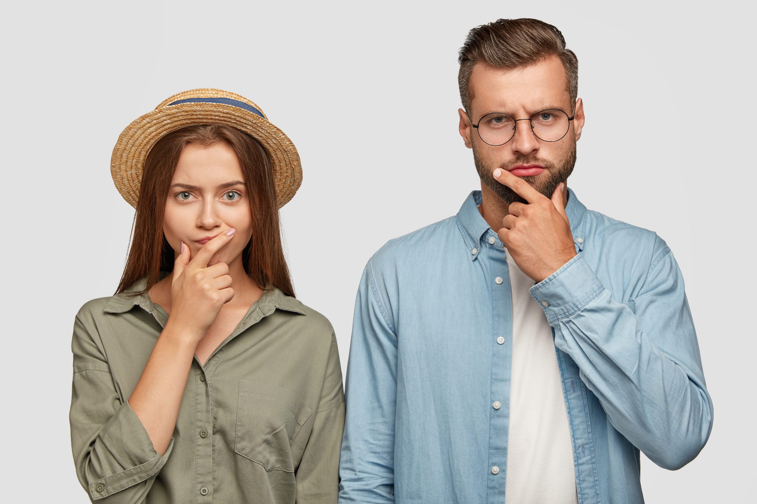 Photo of thoughtful confused female and male coworkers keep hands on chins, think how solve problem with debts, dressed in fashionable shirts, model in studio togeher. Hmm, let us think for moment